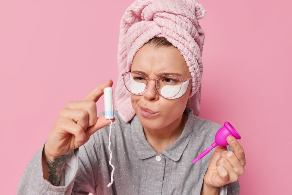 Serious young woman examines two feminine hygiene products for menstruation holds tampon and menstru